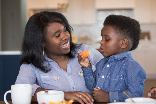 Boy sitting in his mom's lap eating breakfast