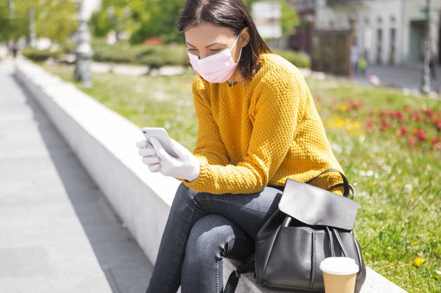 Young Woman With Face Mask Using Smart Phone drinking coffee in city