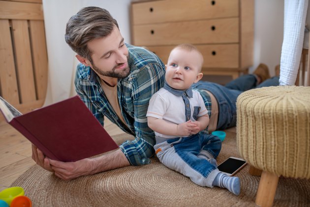 Father in a checkered shirt holding a book and smiling to his little baby boy