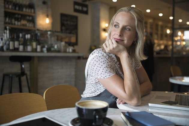 Smiling pensive woman using laptop, looking over shoulder in cafe