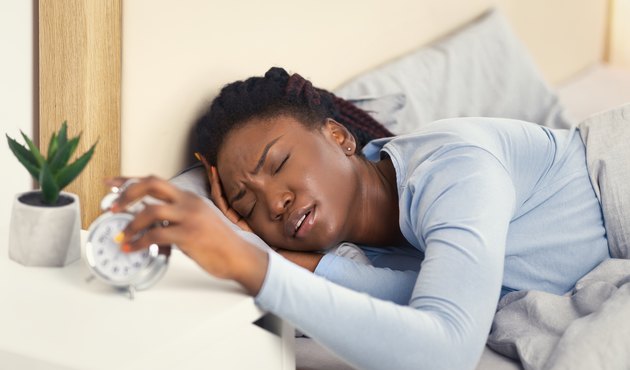 Woman Turning Off Alarm-Clock Touching Head Waking Up In Bed