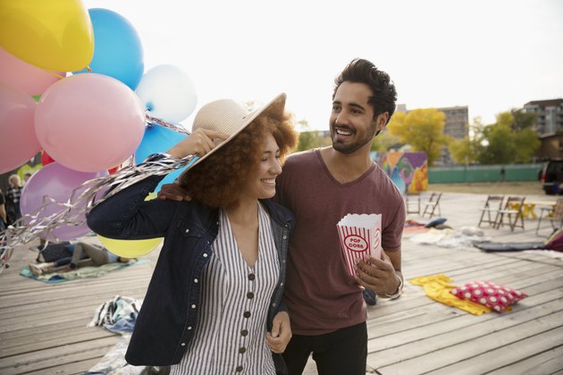Playful young couple with popcorn and balloons in urban park