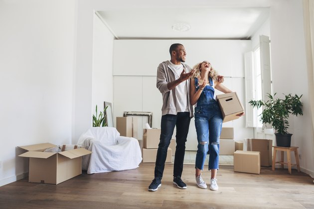 Full length of couple laughing while standing in new home
