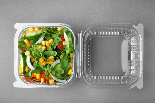 Plastic container with salad on grey background
