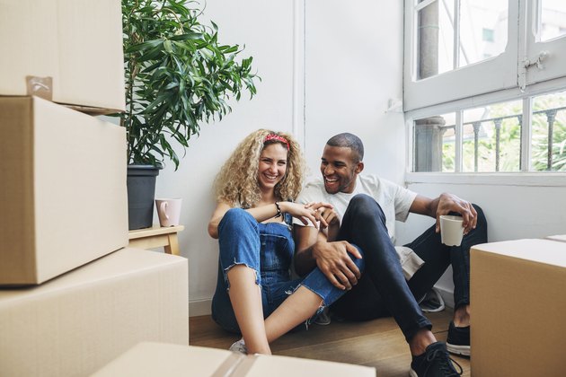 Happy couple talking while having drinks by wall in new house