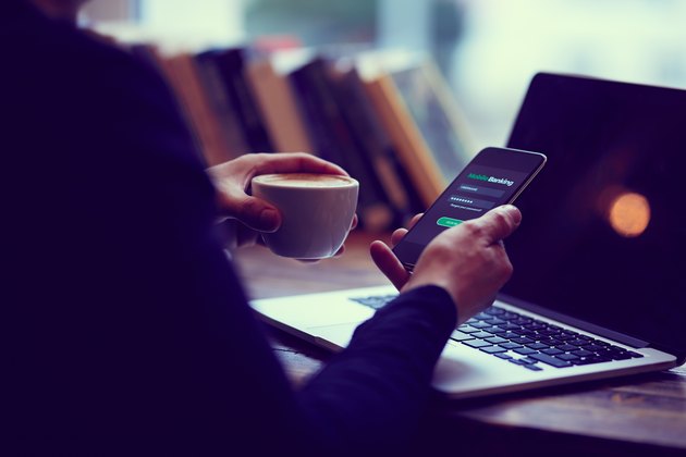 Man holds mobile phone with internet banking and coffee cup