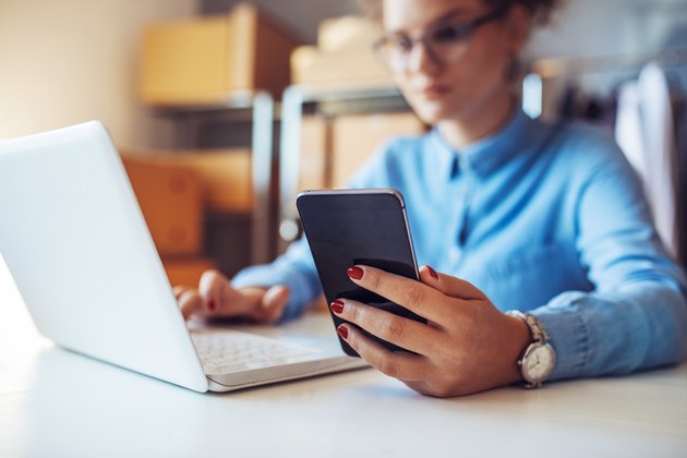 Smiling businesswoman working and using phone in office. Small business entrepreneur looking at her mobile phone and smiling.