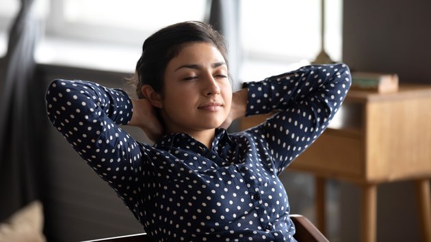 Calm indian lady rest at home office hands behind head