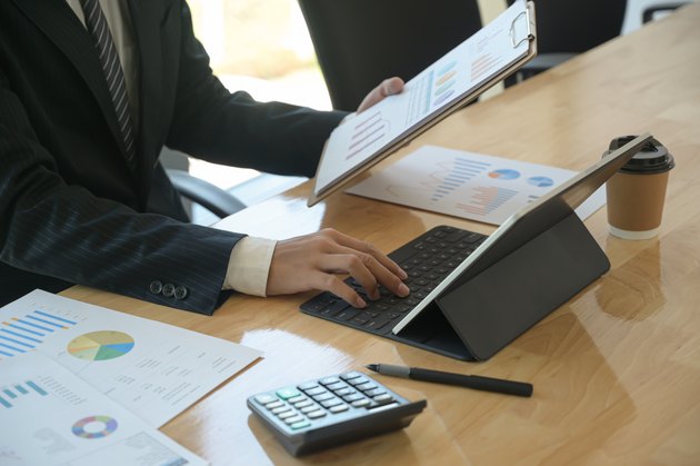 Young executives are checking company earnings. He uses tablet and check the data from chart.