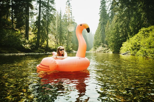 Portrait of laughing woman floating down river on inflatable pink flamingo