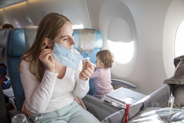 concept trip with a child to Asia, fear of coronavirus covid-19. young beautiful mother in an airplane chair puts on a medical respiratory mask. a cute baby is sitting next to her