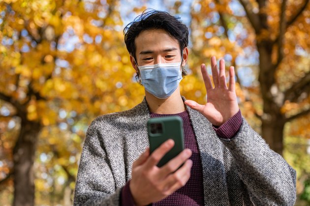 Portrait of young man smiling behind the mask while using a mobile phone
