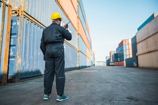 Foreman worker working checking at Container cargo harbor holding radio walkie-talkie to loading containers. Dock male staff business Logistics import export shipping concept.