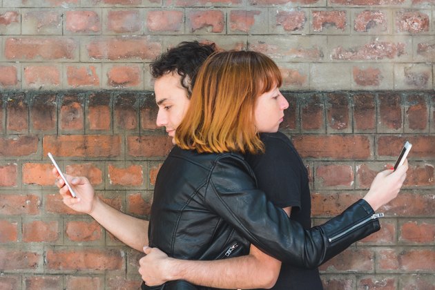 Young couple hugging while each using their smartphone.