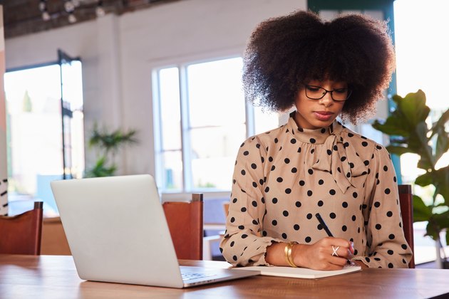 Young businesswoman writing notes and working on a laptop in a cafe