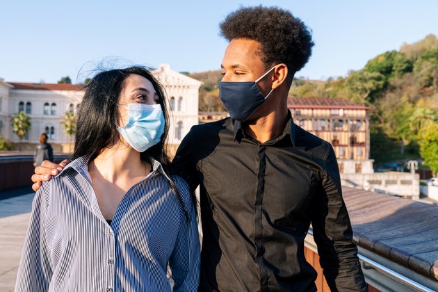 Portrait of a young couple walking down the street embracing a happy blue sky on Valentine's Day with a face mask due to the 2020 covid-19 coronavirus pandemic