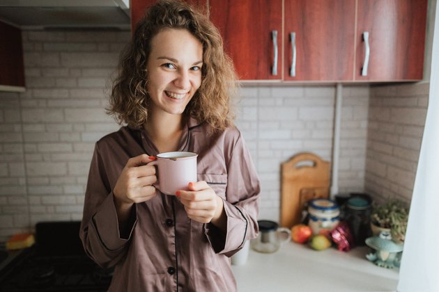 A young beautiful woman drinks a tea or coffee in the domestic kitchen in the morning