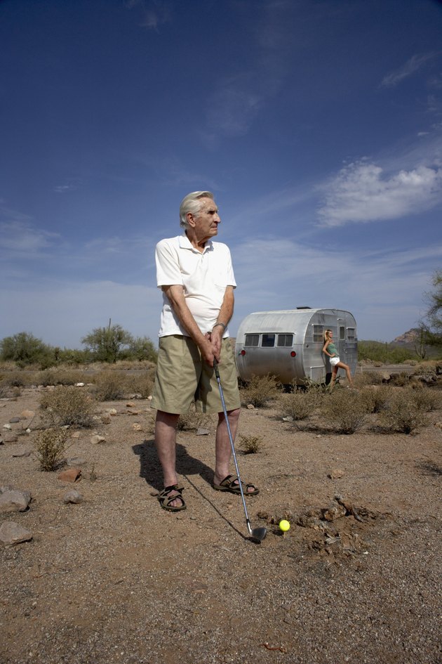 Man playing golf in desert and teenage girl (14-15) leaning on trailer in background