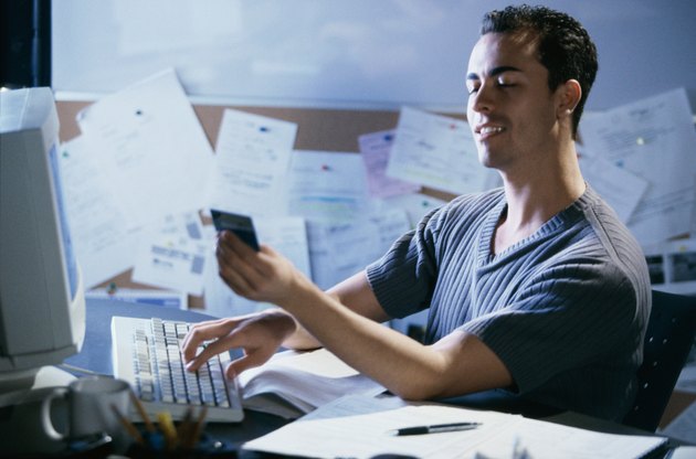 Side profile of a young man working on a computer holding a credit card