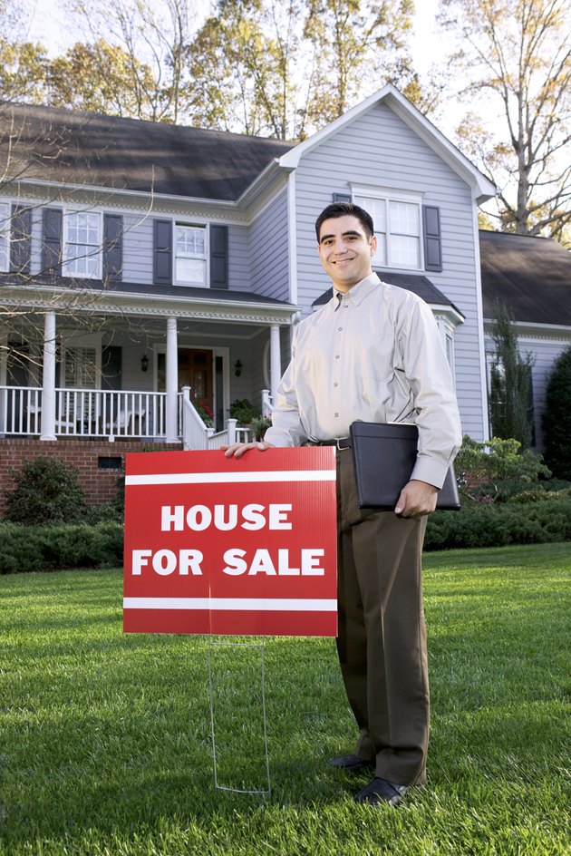 Man posing by house for sale sign