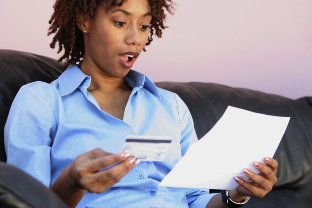 Close-up of a young woman holding a credit card reading a bill