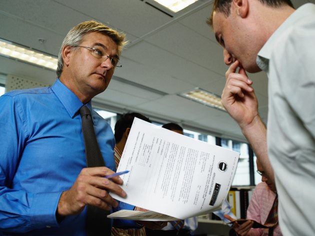 Two businessmen in office, one holding paperwork