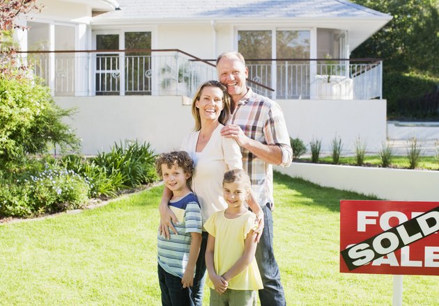 Family standing in front yard of new house next to sold sign