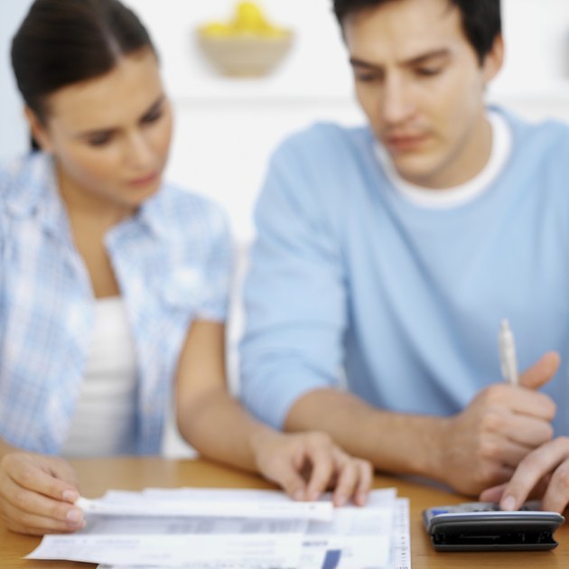 Couple working on documents at desk, focus on hand and calculator