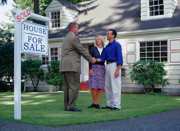 Real estate agent and couple standing in front of sold house