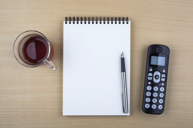 Open notebook and black phone on wooden texture