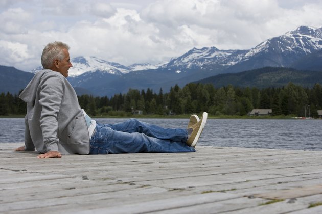 Senior man sitting on pier, looking at view, mountain range in background