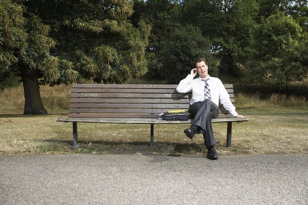 Businessman sitting on park bench, using mobile phone