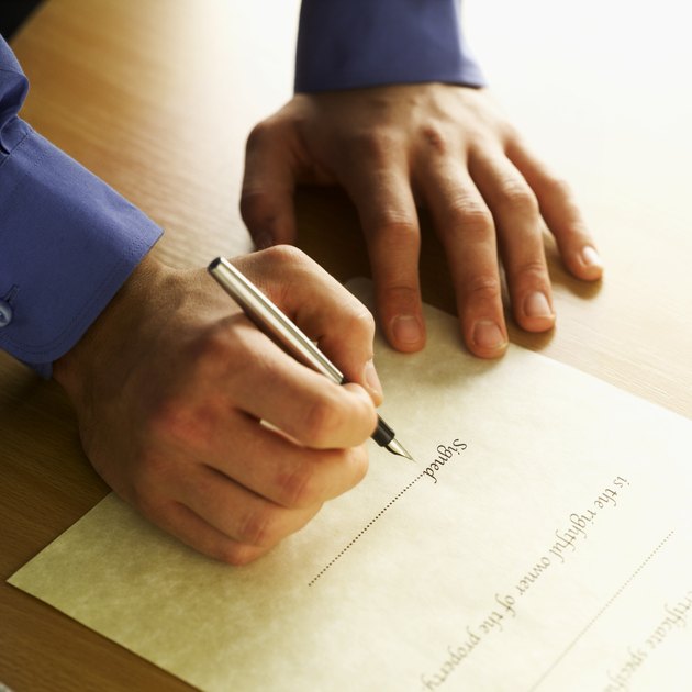 Close-up of man's hands signing house deeds with pen