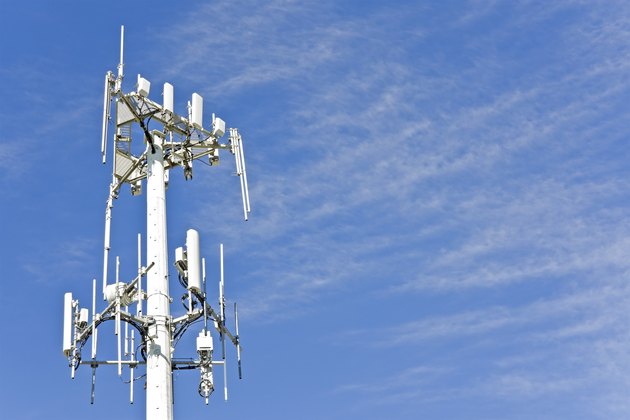 Cell phone telecommunication tower with wispy clouds, blue sky.