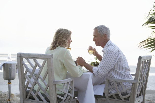Mature couple holding hands sitting at restaurant on beach