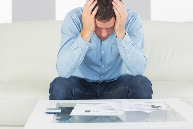 Frustrated casual man sitting on couch paying bills