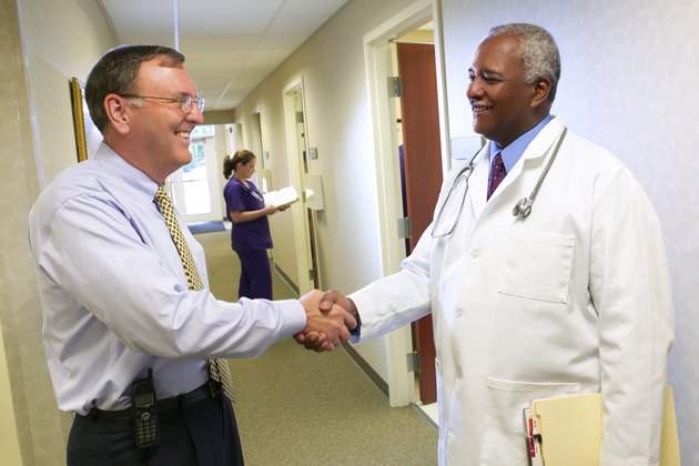 An administrator and doctor shake hands in the hall of a doctor's office