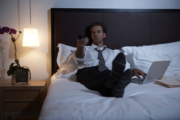 Businessman lying on bed using laptop and remote control
