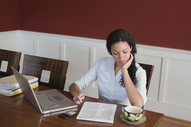 Woman Working on Laptop Computer, Calculator and Tax Documents at Dining Room Table