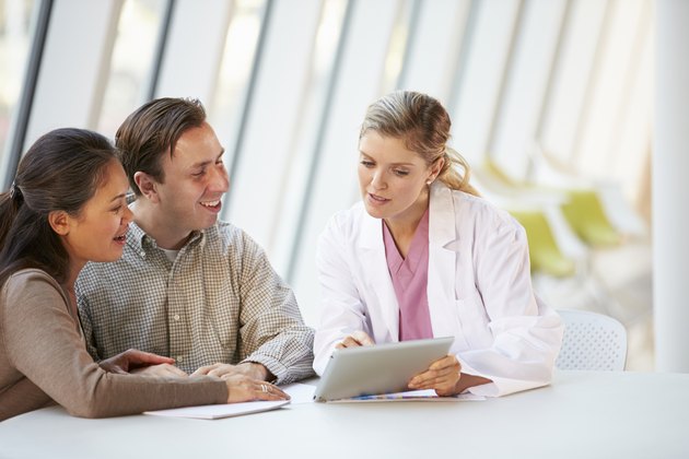 Female Doctor Using Digital Tablet Talking With Patients