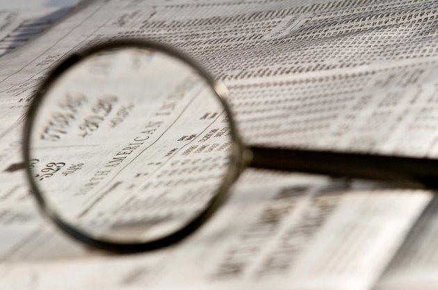 Magnifying glass highlighting investment stock quotes in business section of newspaper.