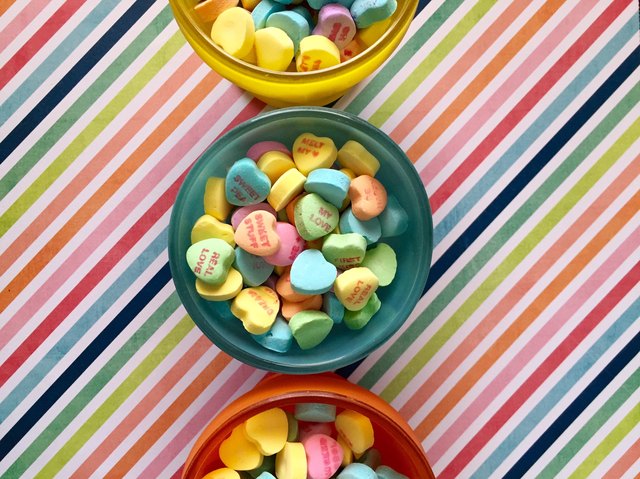Conversation hearts in bowl against rainbow striped background