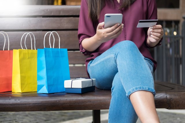 Woman paying with credit card on phone with gift bags next to her