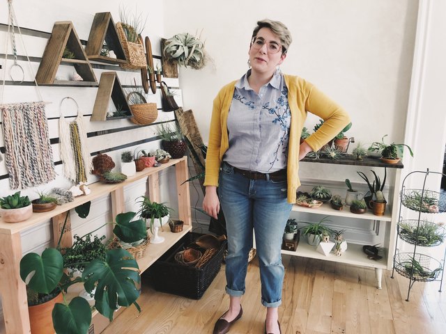 Woman in yellow cardigan stands in front of houseplants