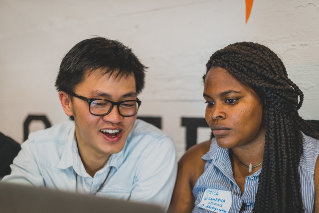 Man and woman sitting at computer; she looks unimpressed as he explains something