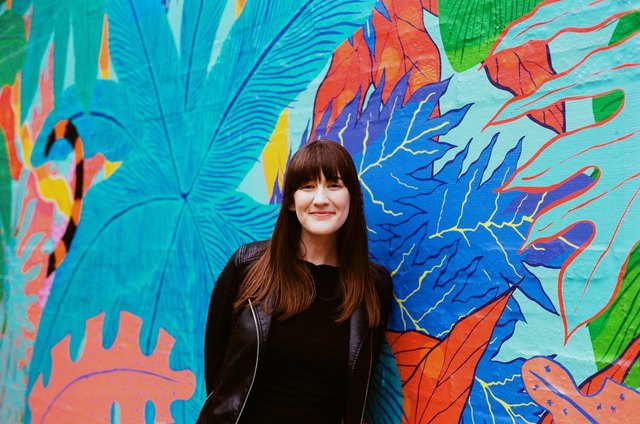 Woman in black poses in front of colorful mural of leaves