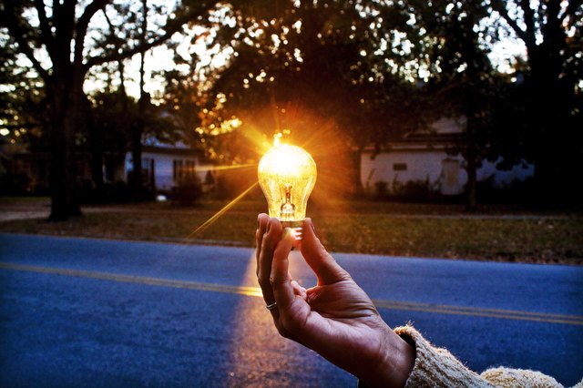 Unseen person holds lightbulb in front of setting sun outdoors