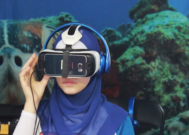 Young hijabi in aquarium wearing VR headset