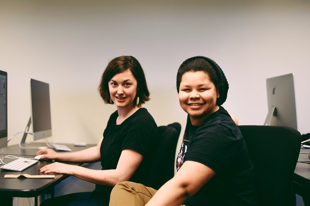 Two young women smiling in front of computer station