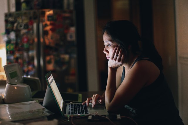 East Asian woman working on laptop in dim room